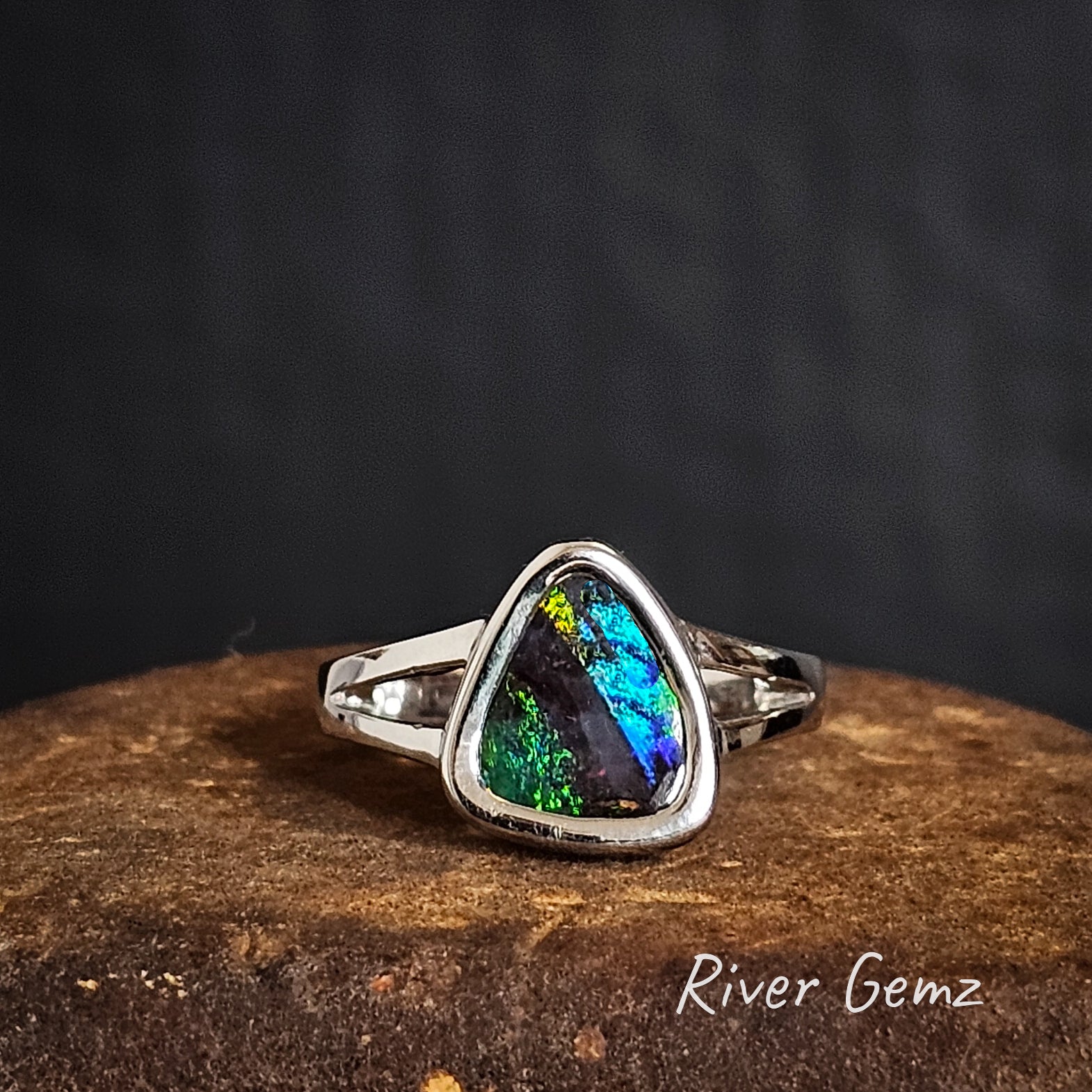 Silver ring with a triangular black boulder opal on a dark background, branded 'River Gemz'.