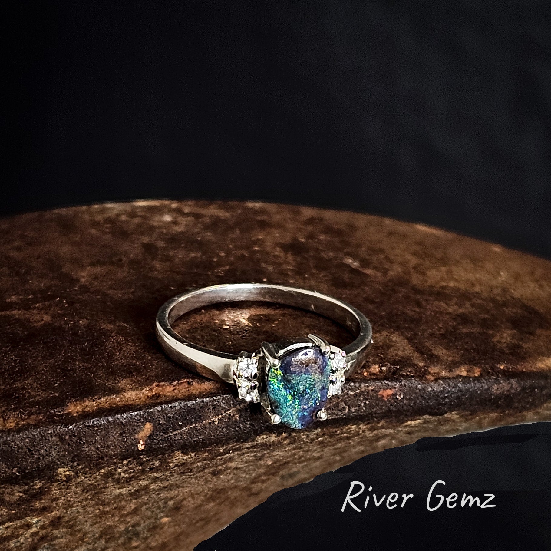 Silver ring with a colourful boulder opal and 4 white topaz stones on a dark background, featuring the brand 'River Gemz'.
