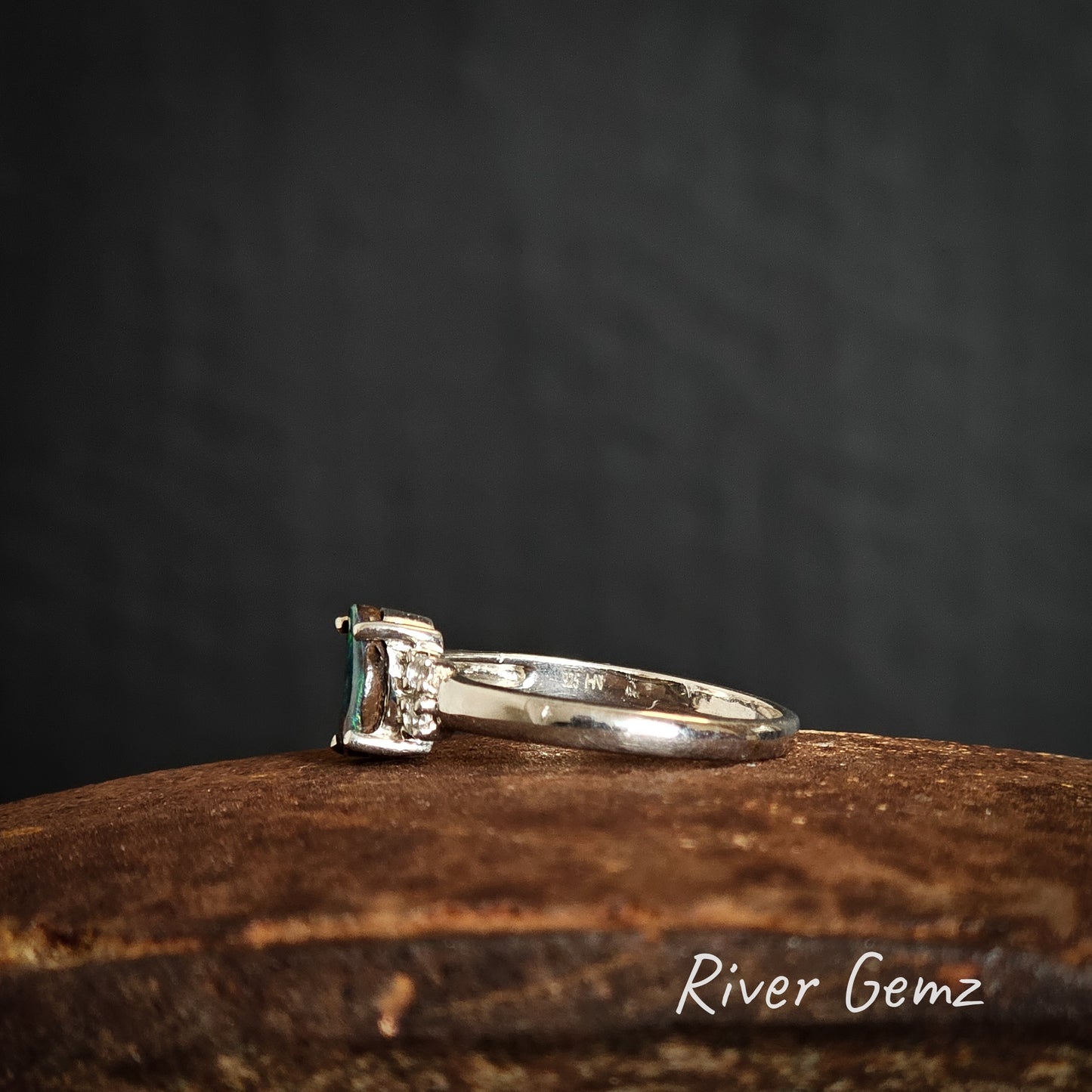 Side view of silver ring with a green gemstone on a rusty surface with 'River Gemz' branding.