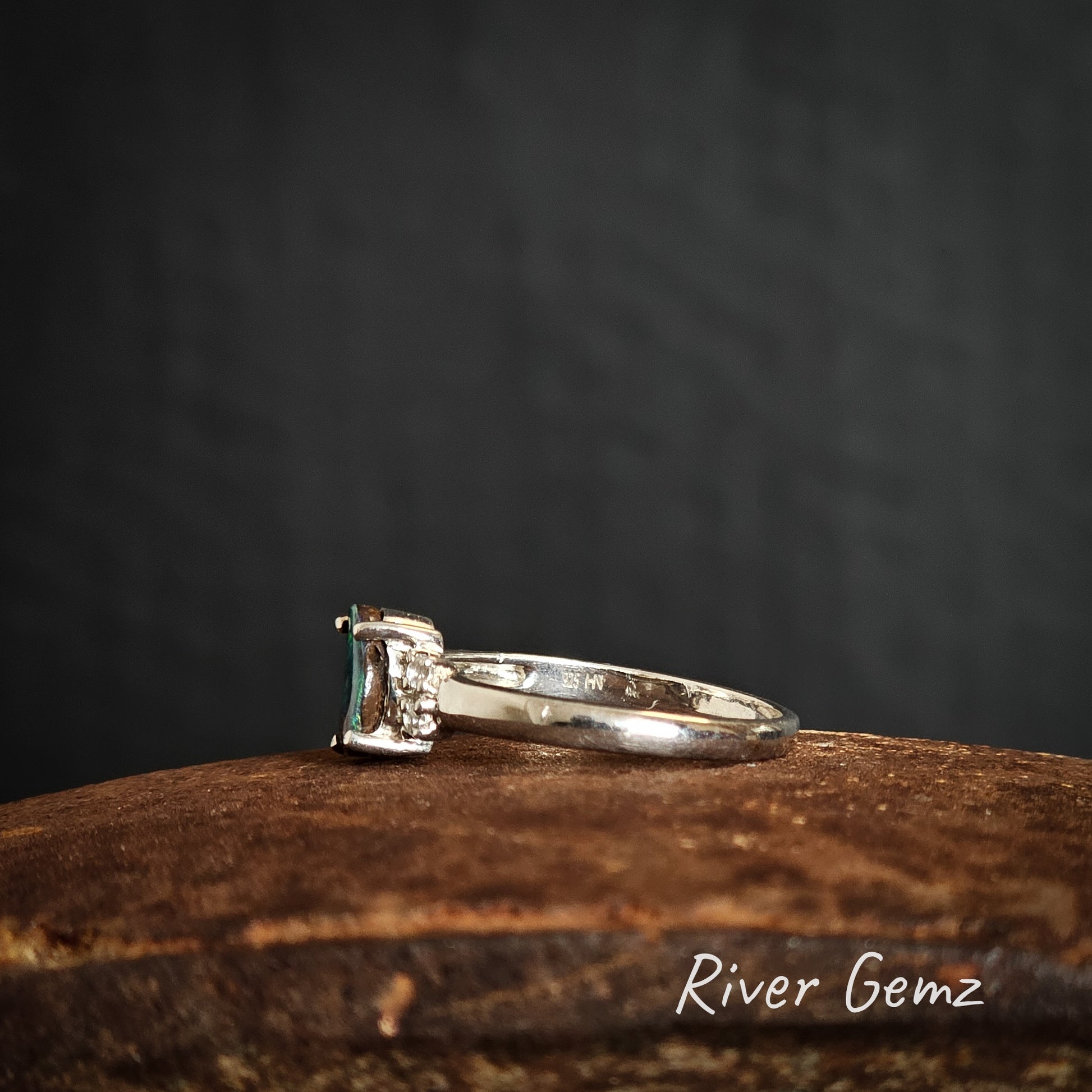 Side view of silver ring with a green gemstone on a rusty surface with 'River Gemz' branding.