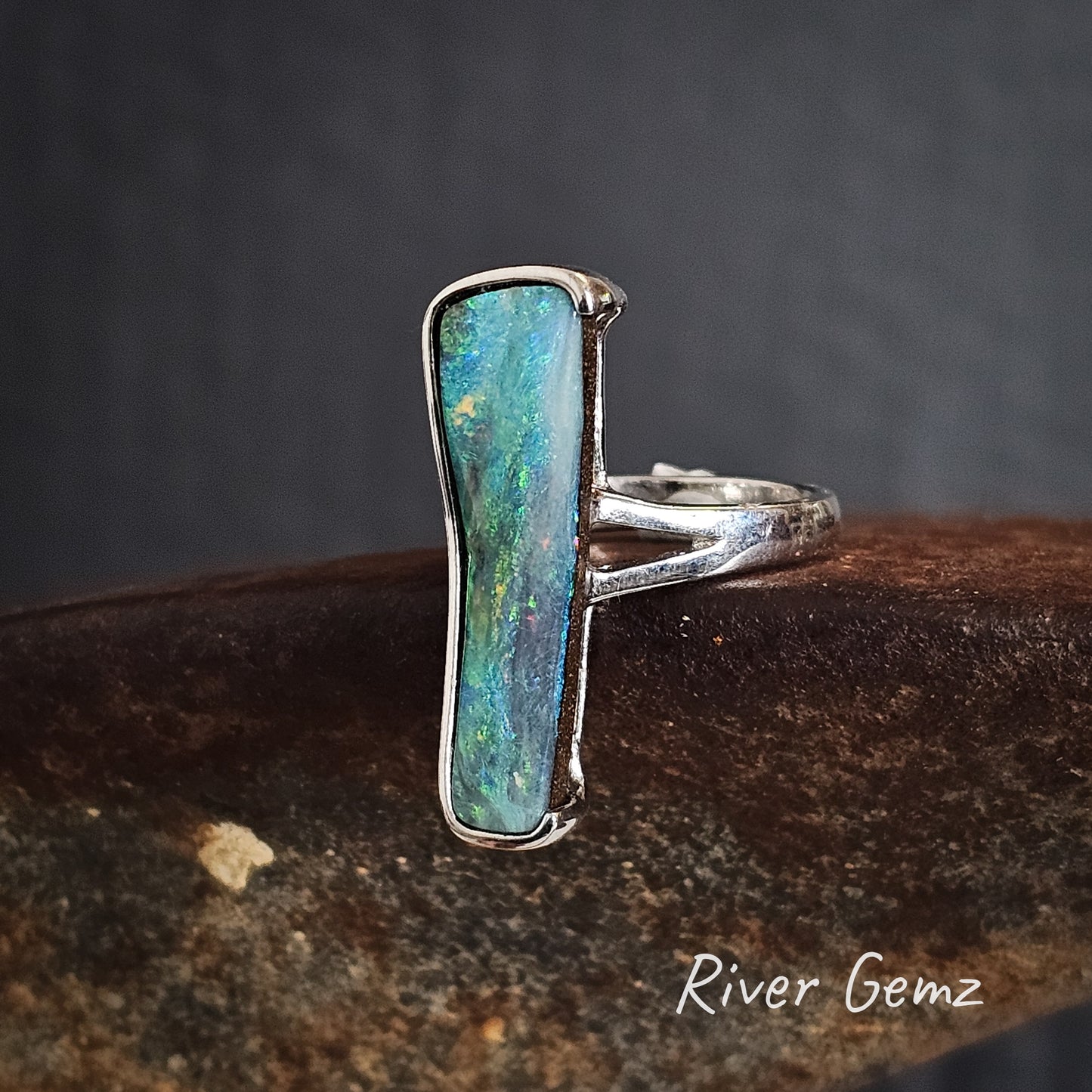 Silver ring with a free-form cut greenish-blue boulder opal on a dark background.