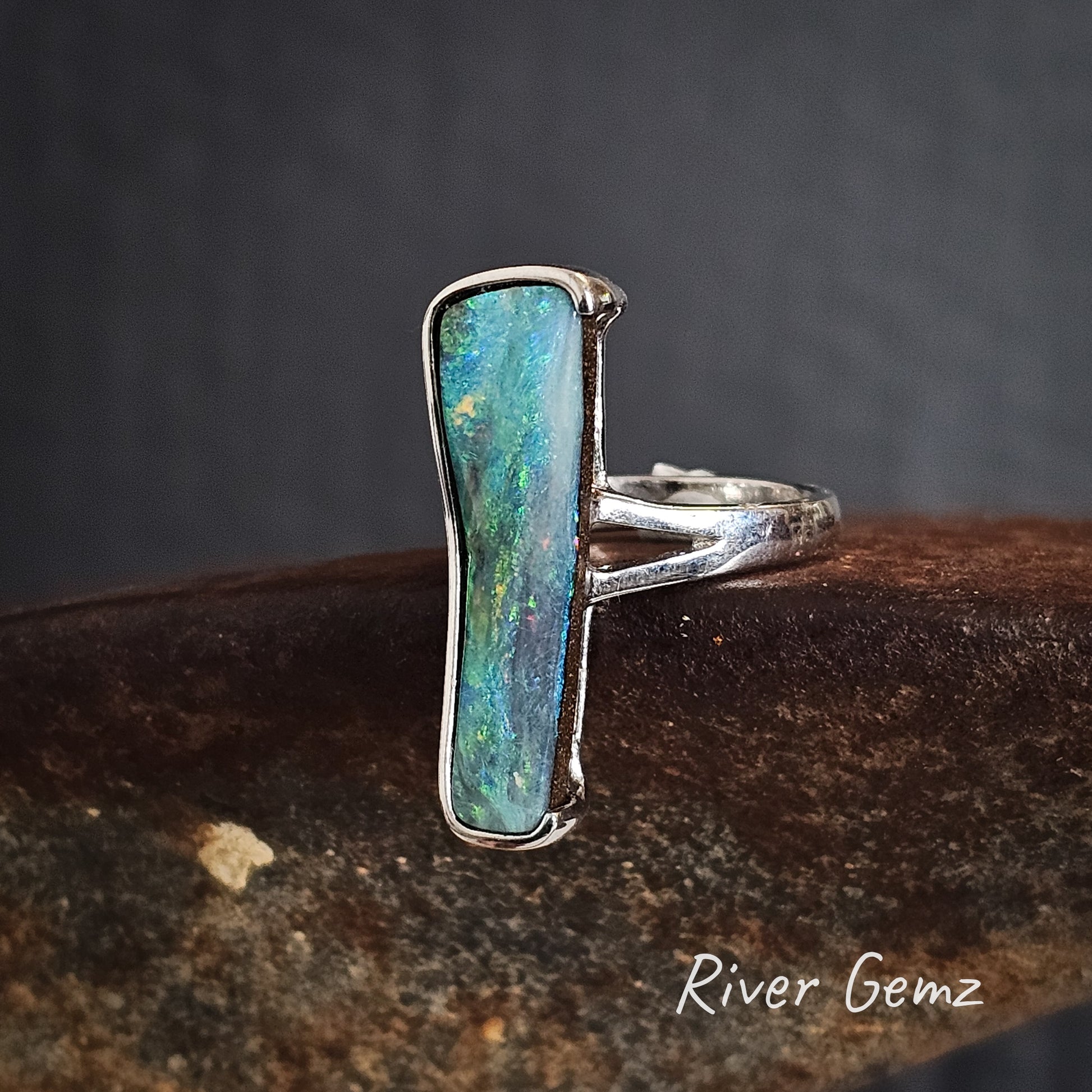 Silver ring with a free-form cut greenish-blue boulder opal on a dark background.
