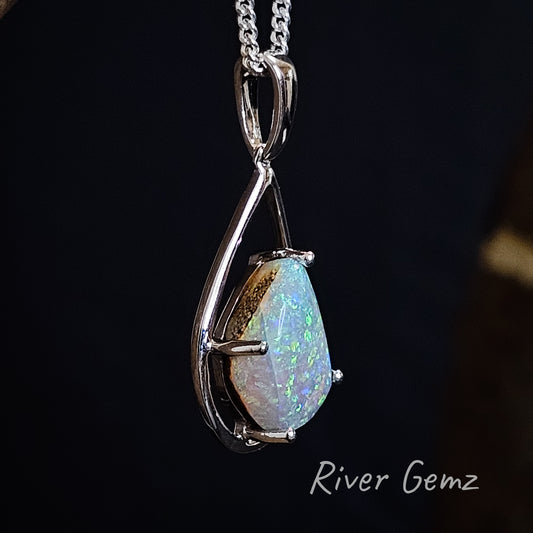 Slightly side on view of vibrant green and blue pipe opal showing the ironstone host rock. Stone is claw set in silver necklace with large bail.