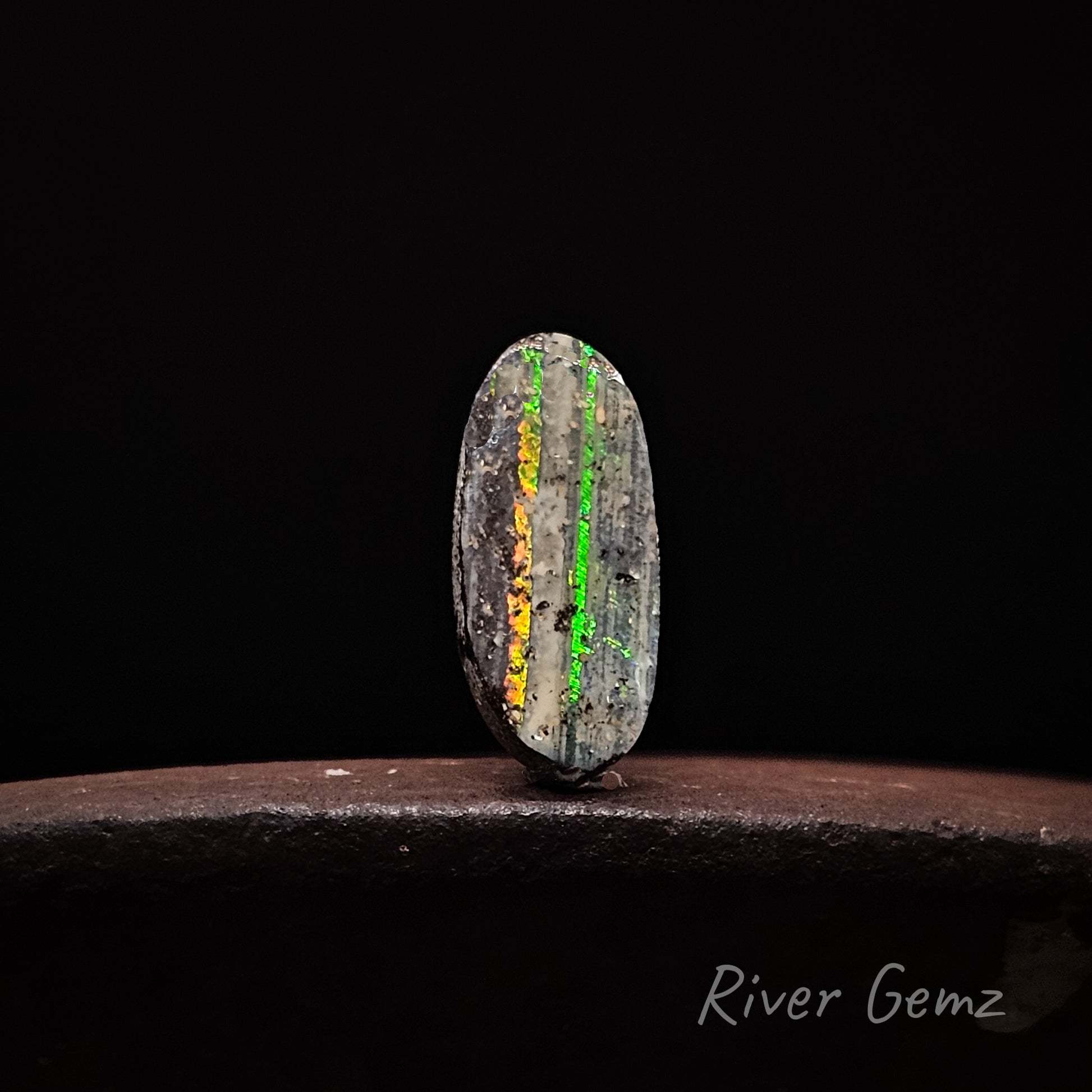Unset boulder opal with two colorful veins on a dark background, labeled 'River Gemz'.