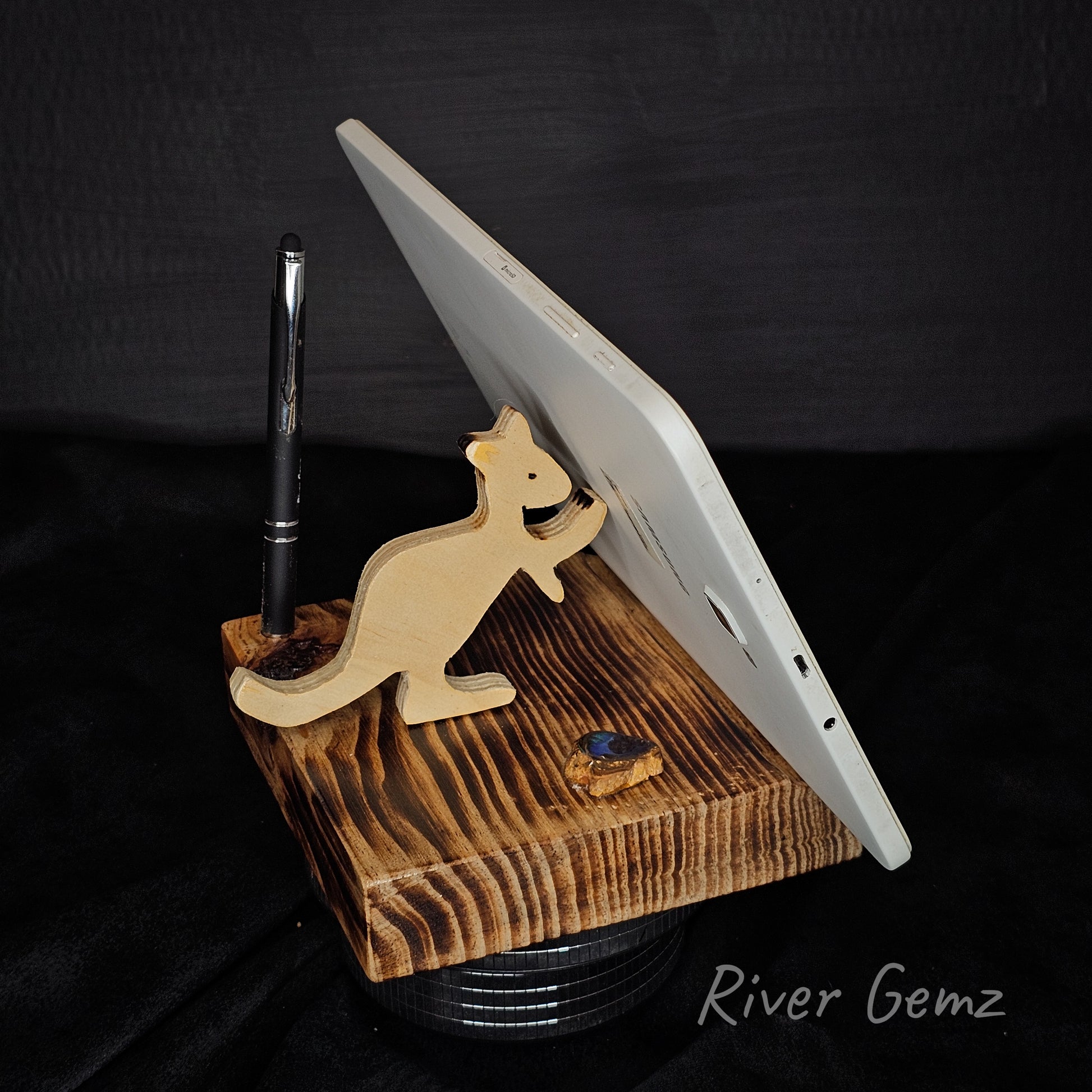 Wooden stand holding a tablet and pen with 'River Gemz' branding on a dark background