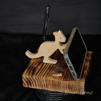 Wooden kangaroo phone stand holding a phone on a dark background