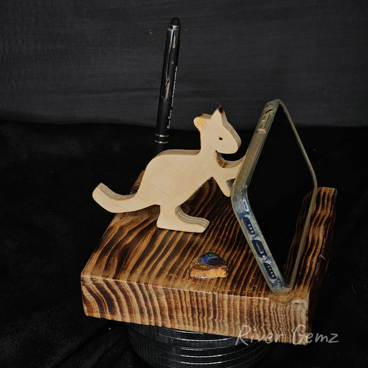 Wooden kangaroo phone stand holding a phone on a dark background