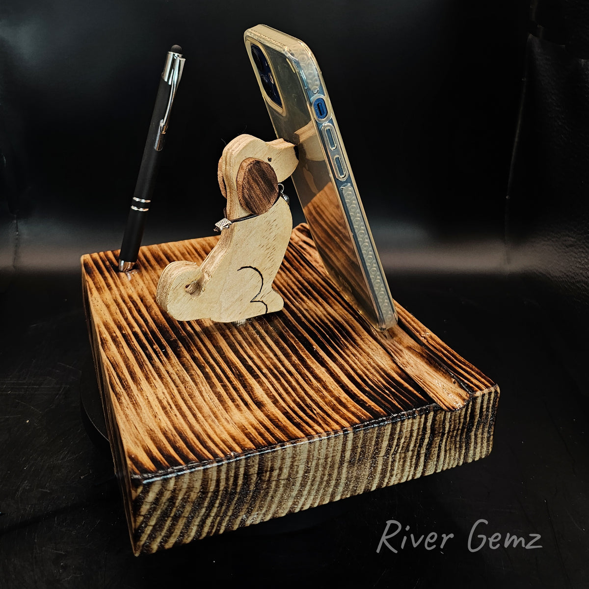 Wooden dog phone/tablet stand. Dog is in sit position with a mobile phone leaning against it's nose.
