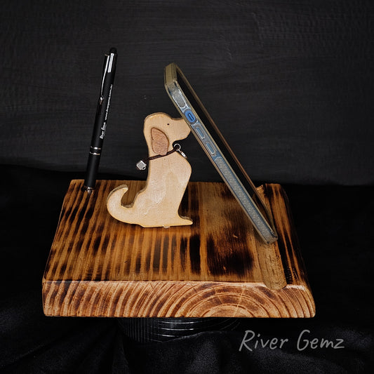 Wooden phone stand with a dog-shaped item and pen on a black background, branded 'River Gemz'.
