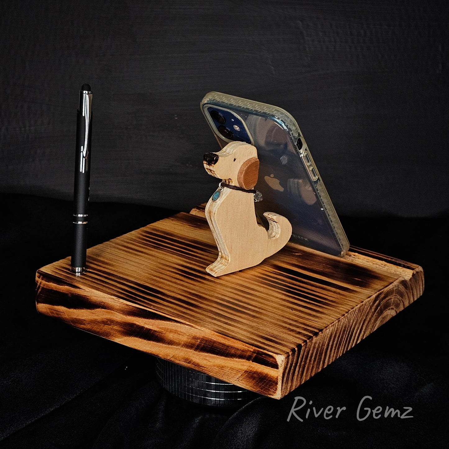 Wooden phone stand with a dog design holding a phone including a stylus/pen  on a dark background.