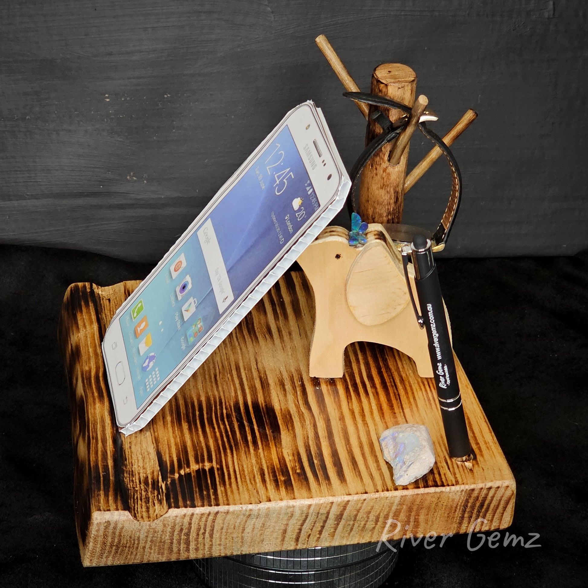 Wooden phone stand with smartphone, pen, and small object on a dark background