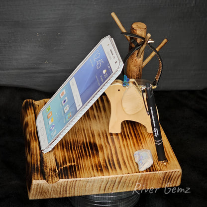 Wooden phone stand with smartphone, pen, and small object on a dark background