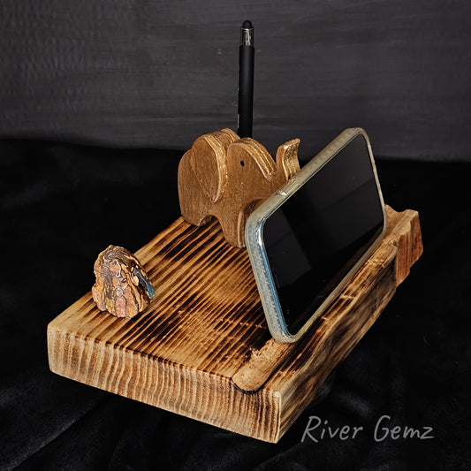 Wooden elephant phone stand holding a smartphone on a dark background with 'River Gemz' branding.