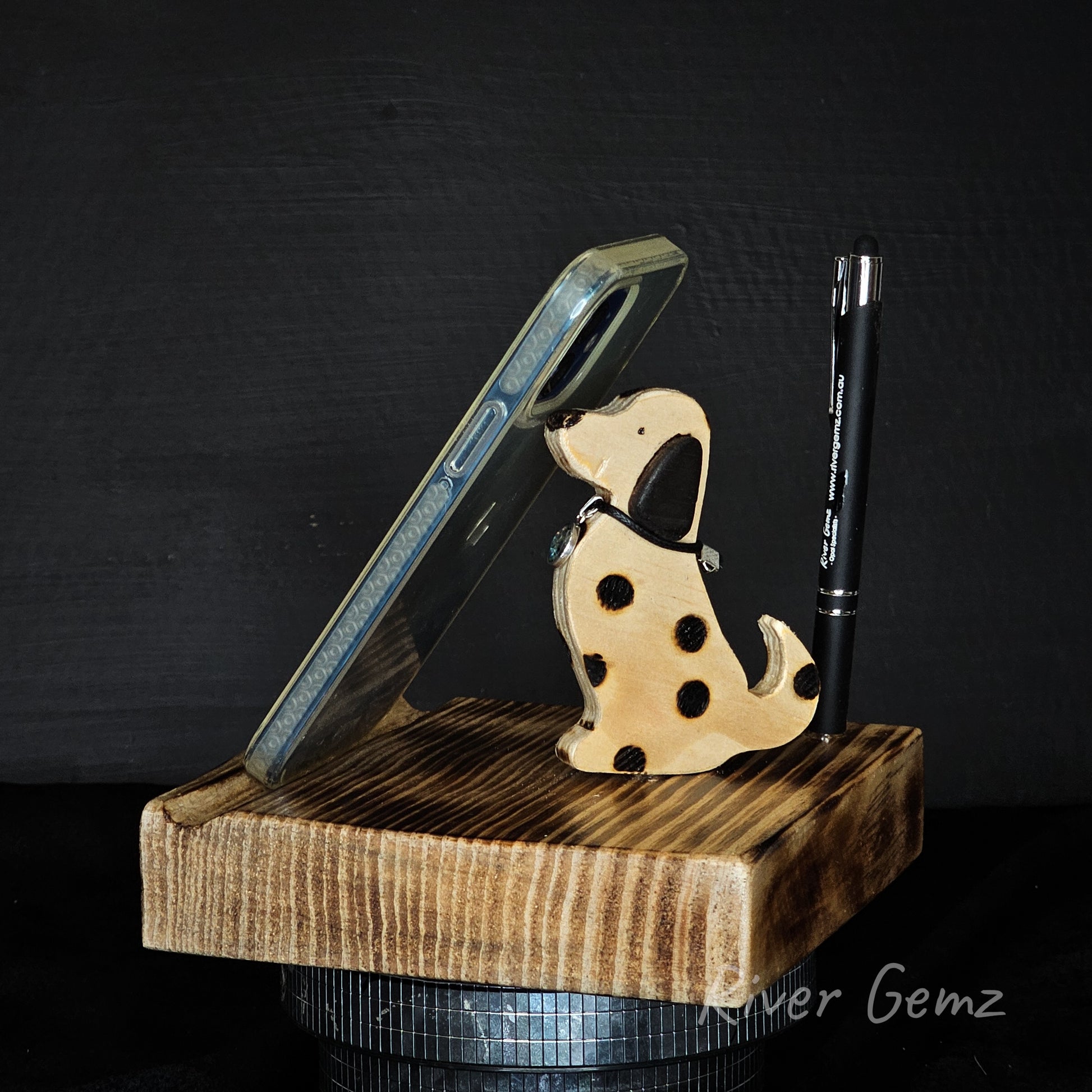 Wooden phone stand with phone, dog-shaped stand, and pen on a dark background