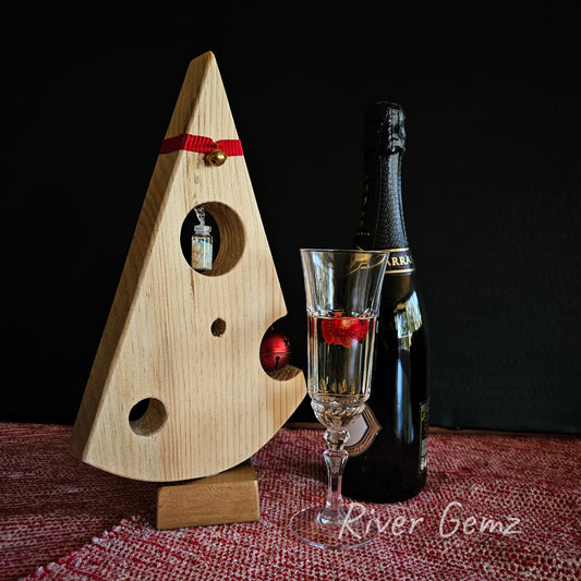 An uncomplicated small wooden Christmas tree in the shape of a piece of Swiss cheese. Photo includes champagne bottle and glass to show the festive spirit.