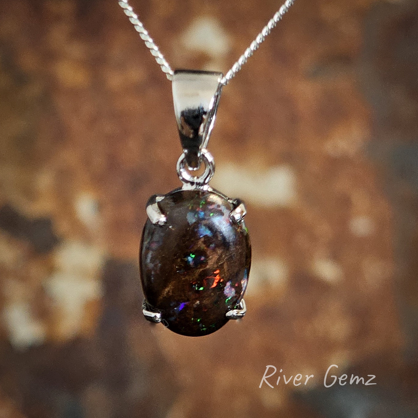 Oval shaped dark boulder opal with flicks of colour held with 4 claws in silver necklace with large bail.