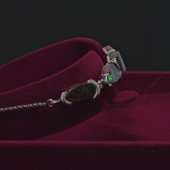 Silver bracelet with 5 dark opals in a moroon velvet box rotating 180 degrees in this video.