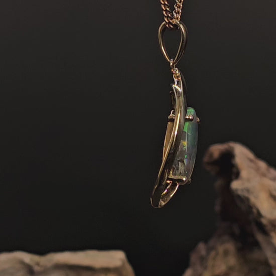 Video showing the black opal in gold pendant rotate 200 degrees against a dark background.