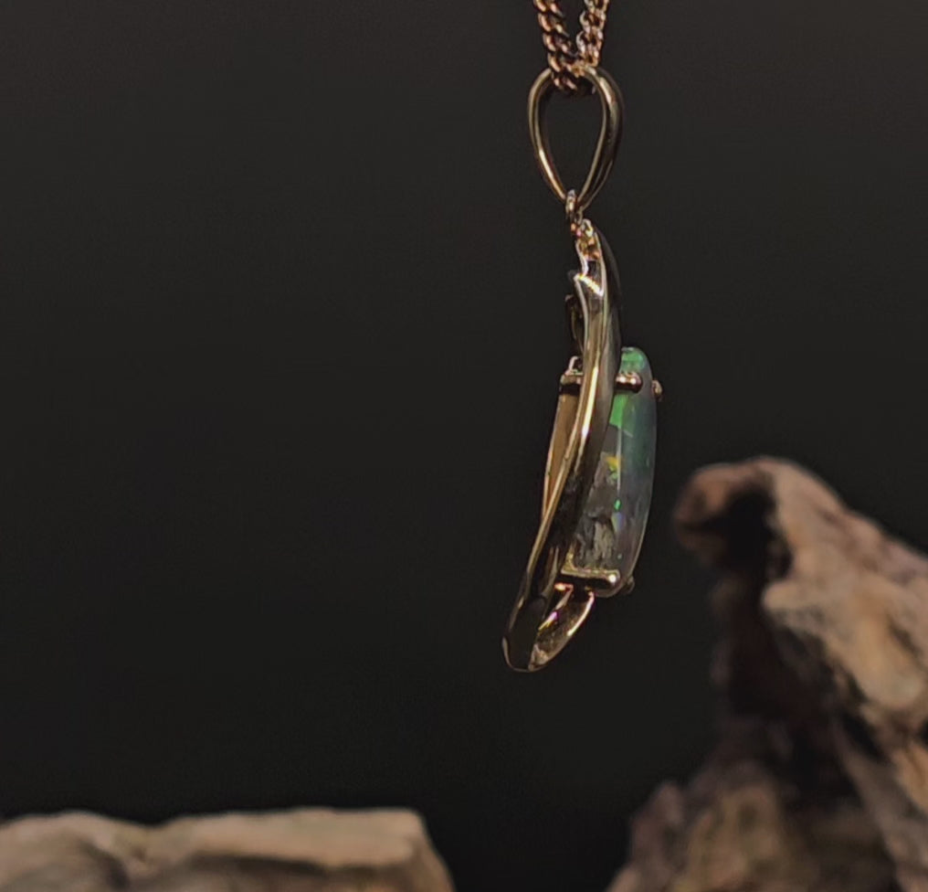 Video showing the black opal in gold pendant rotate 200 degrees against a dark background.