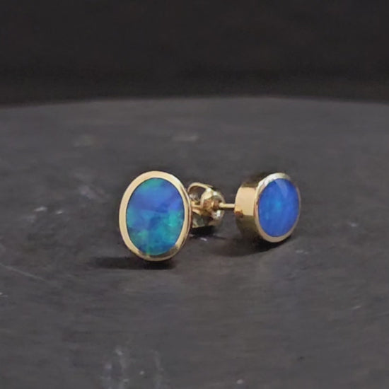 Dark blue and green black crystal opal set in yellow gold stud earrings shown turning 200 degrees in video format.