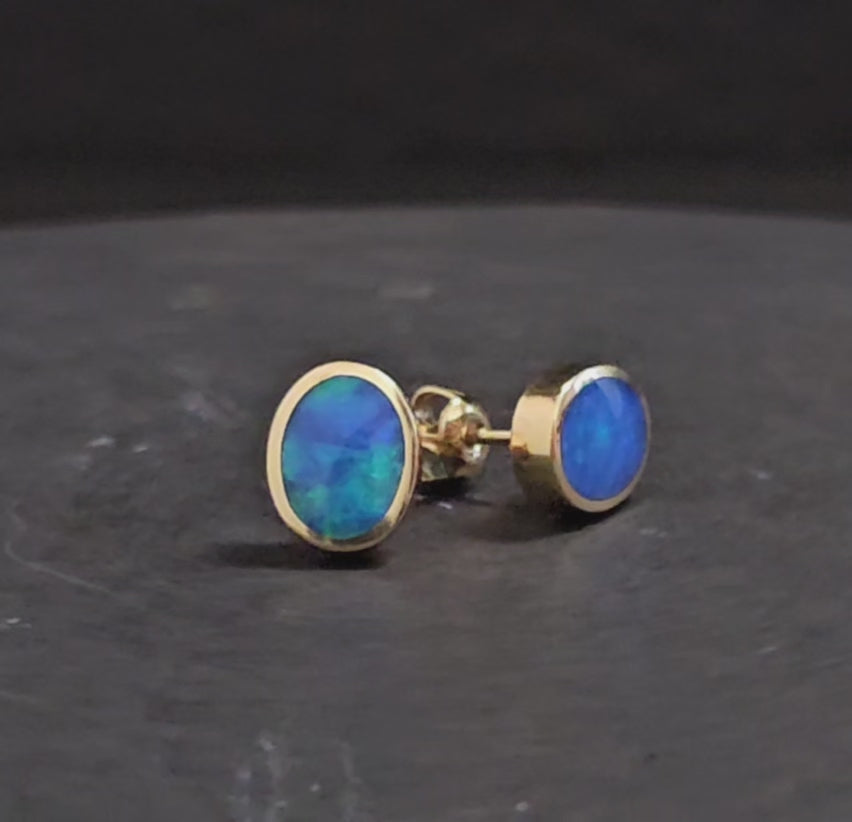 Dark blue and green black crystal opal set in yellow gold stud earrings shown turning 200 degrees in video format.