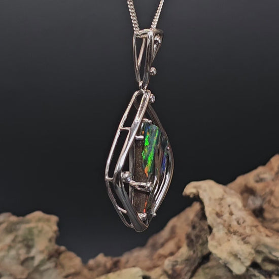 Video showing large multi-coloured dark opal rotate 200 degrees showing all faces of the opal.
