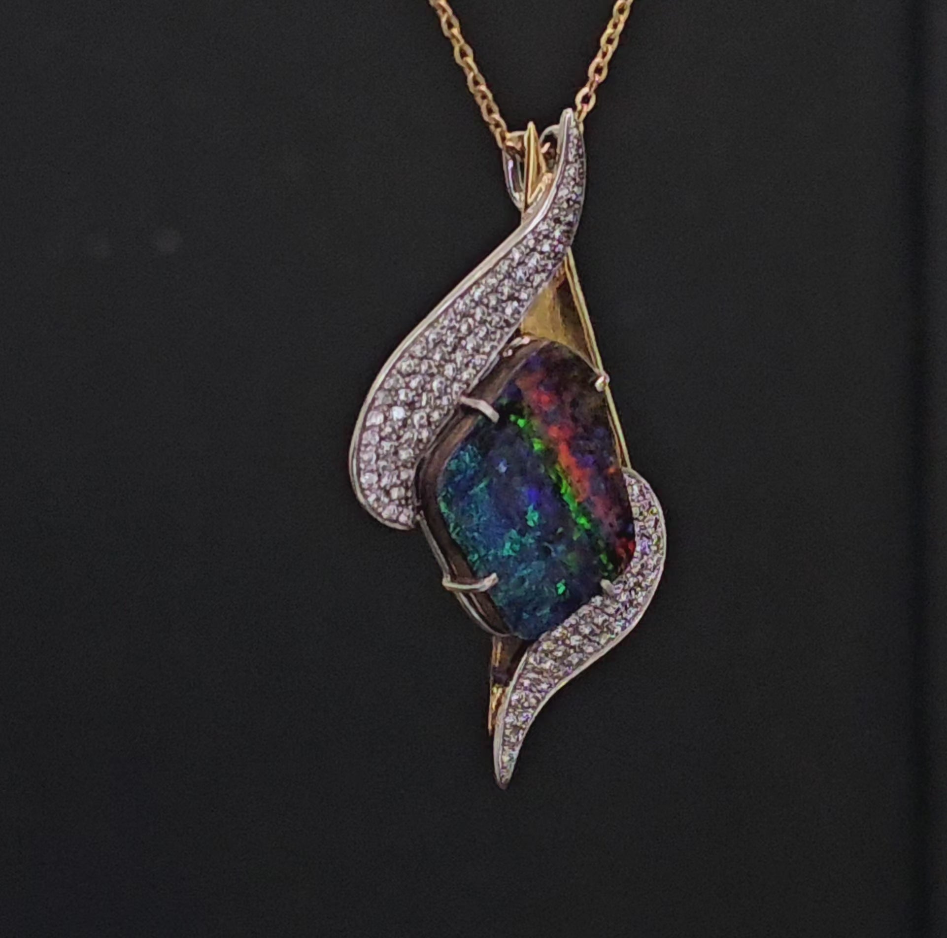 Yellow gold and platinum necklace adorned with lots of diamonds and a colourful dark opal as the centrepiece shown rotating in video footage.