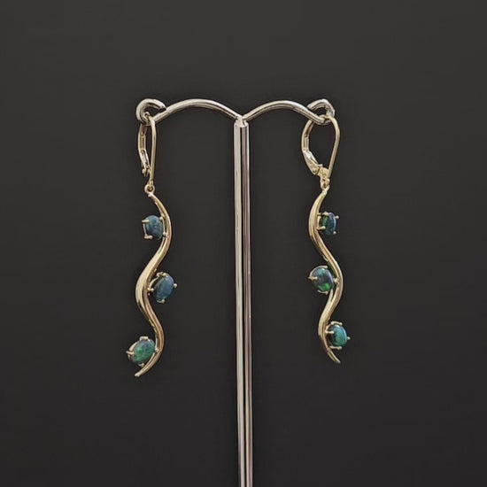 3 dark opals claw set in long dangly gold earrings. Snake like track design with the 3 opals alternating sides of the track.