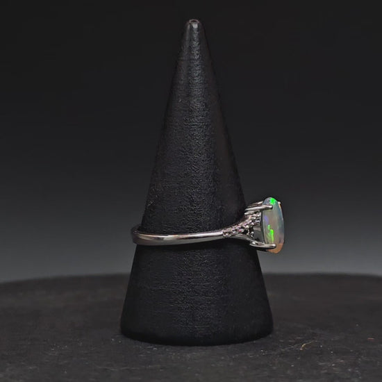 Oval shaped crystal opal set in a silver ring shown rotating on a ring display.