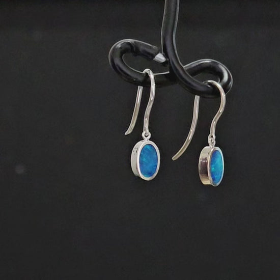 Traditionally set oval shaped blue opals in white gold shepherd hook earrings.