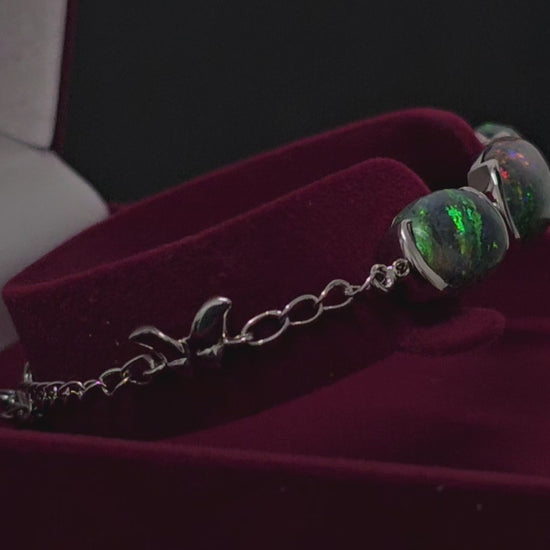 Video showing silver bracelet with 3 dark opals in moroon velvet box spinning 180 degrees.